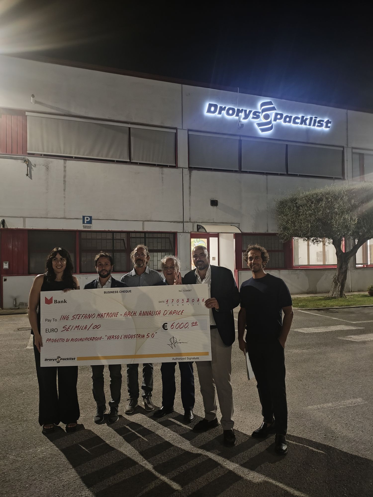 The first-place winners holding their check in front of the Drorys Packlist headquarters, illuminated at night